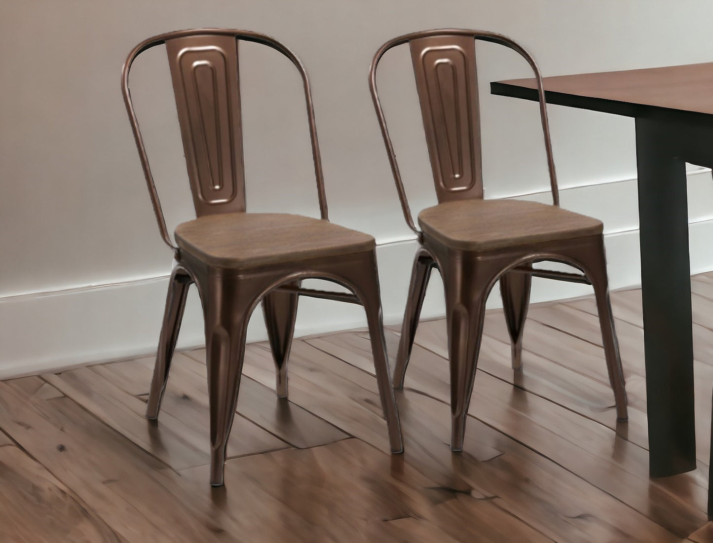 Two brown metal chairs in front of a wooden table on a wooden floor.