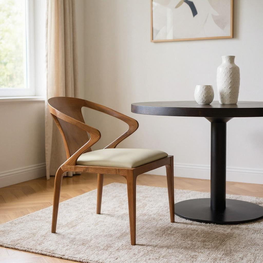 Wooden chair with cream cushion next to a round black table in a room with a window and abstract art on the wall.