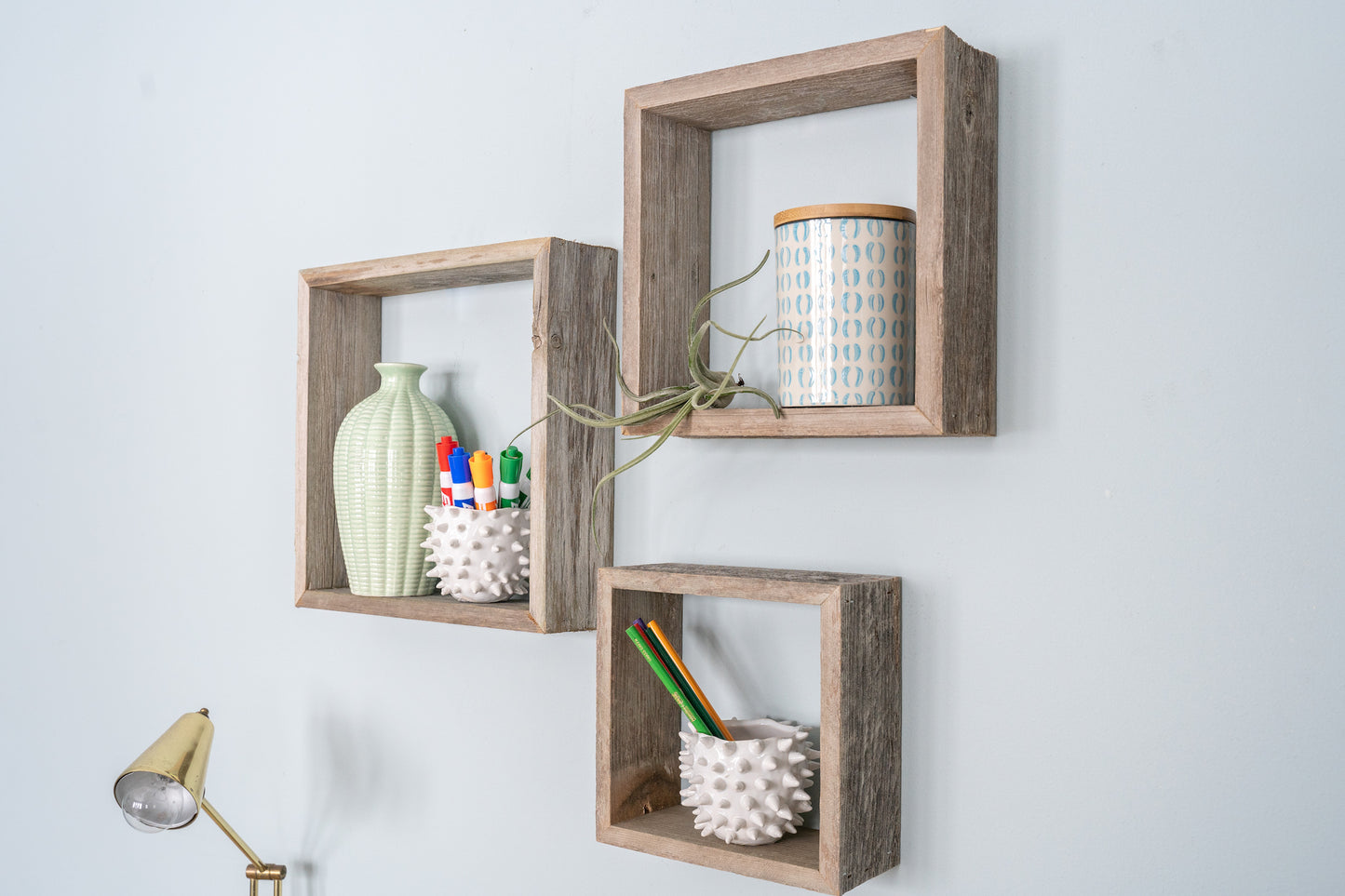 Three wooden square shelves on a white wall with decorative items.