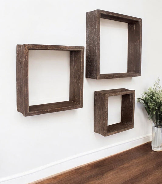 Three wooden square shelves of different sizes on a white wall.