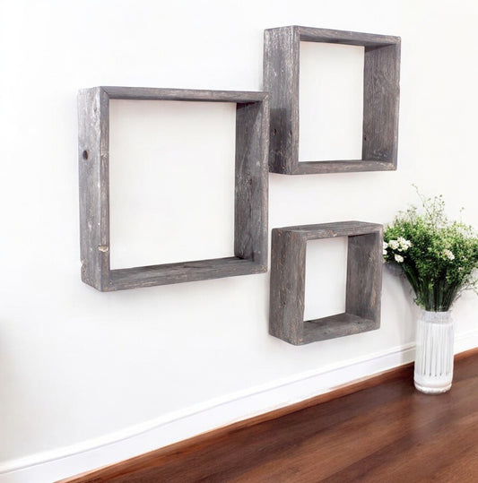 Three square wooden wall shelves on a white wall with a vase of flowers on a wooden floor.