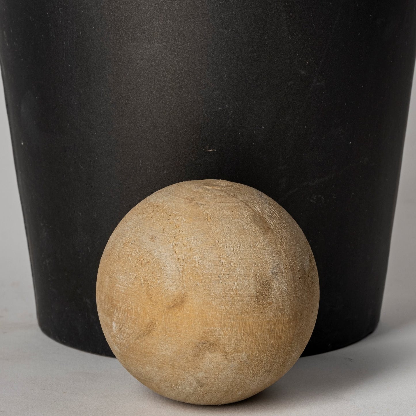 Wooden ball next to a black cylindrical object on a neutral background
