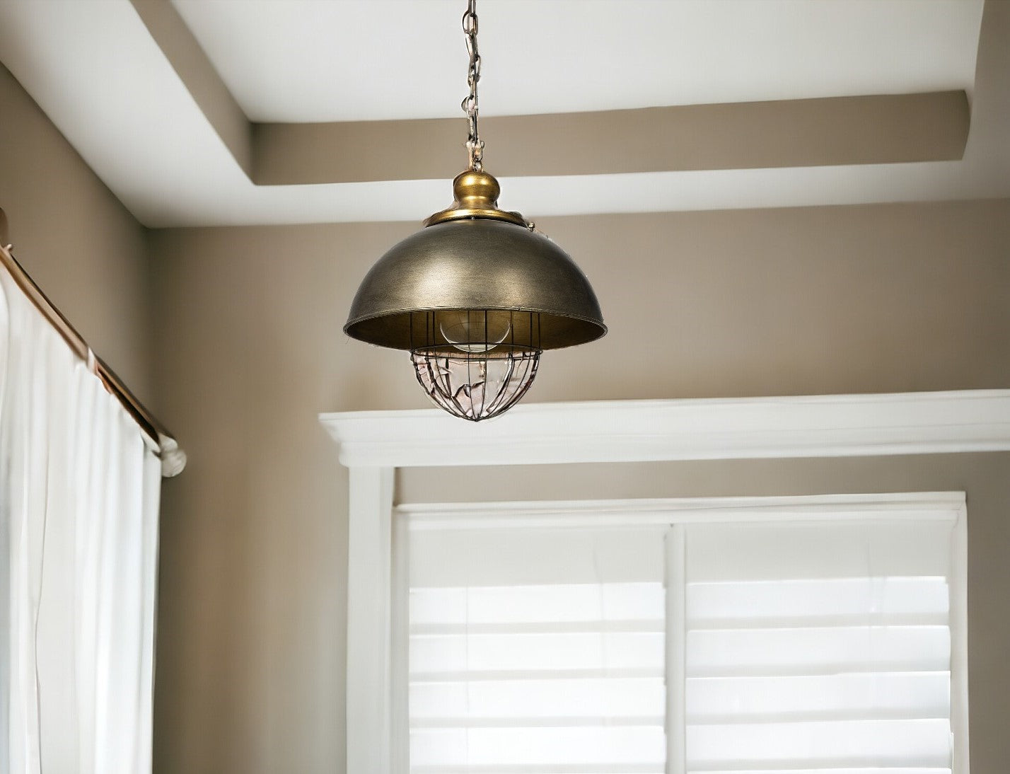 Bronze pendant light hanging in a room with neutral walls and a window.
