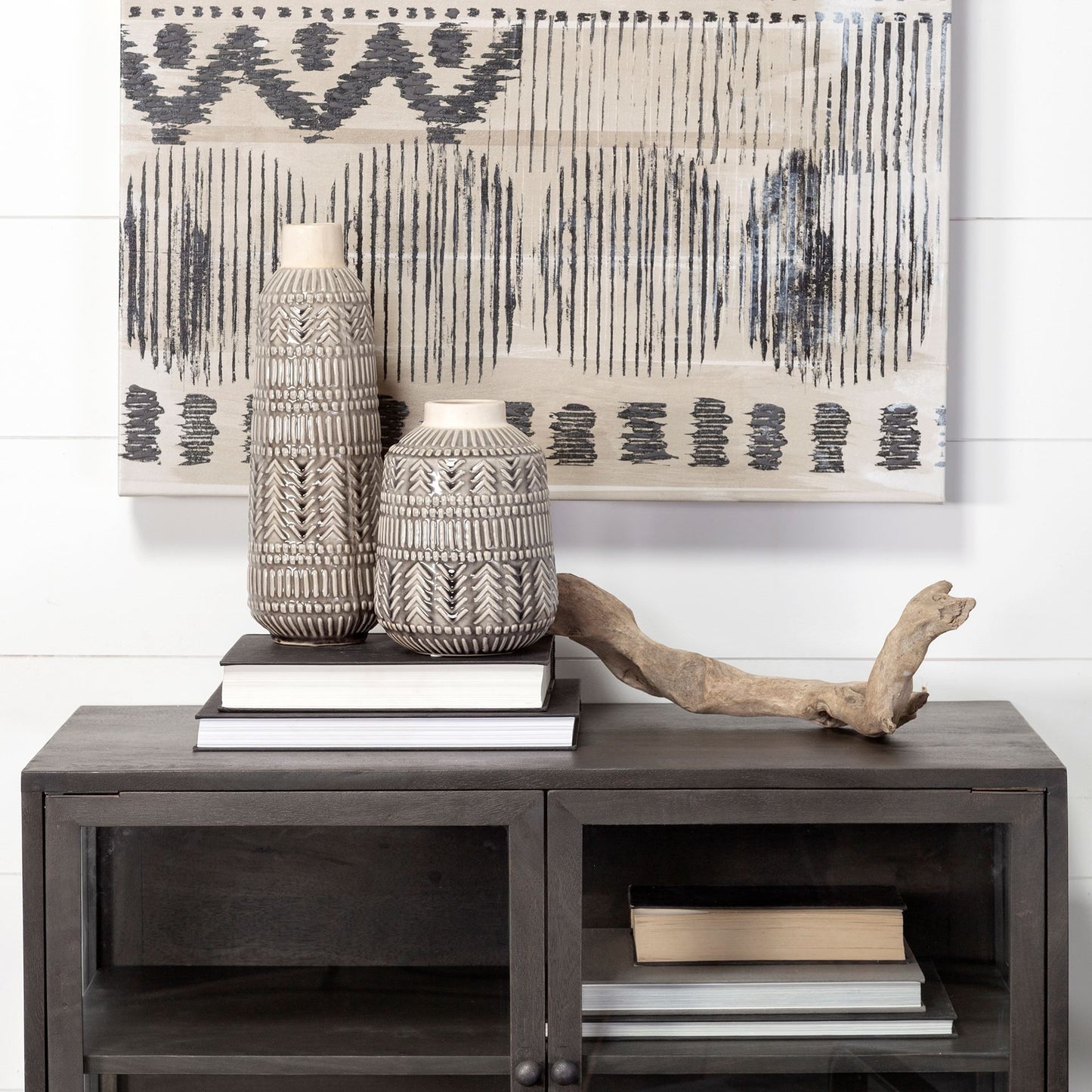 Decorative setup with vases, books, and driftwood on a wooden console table with abstract art in the background.