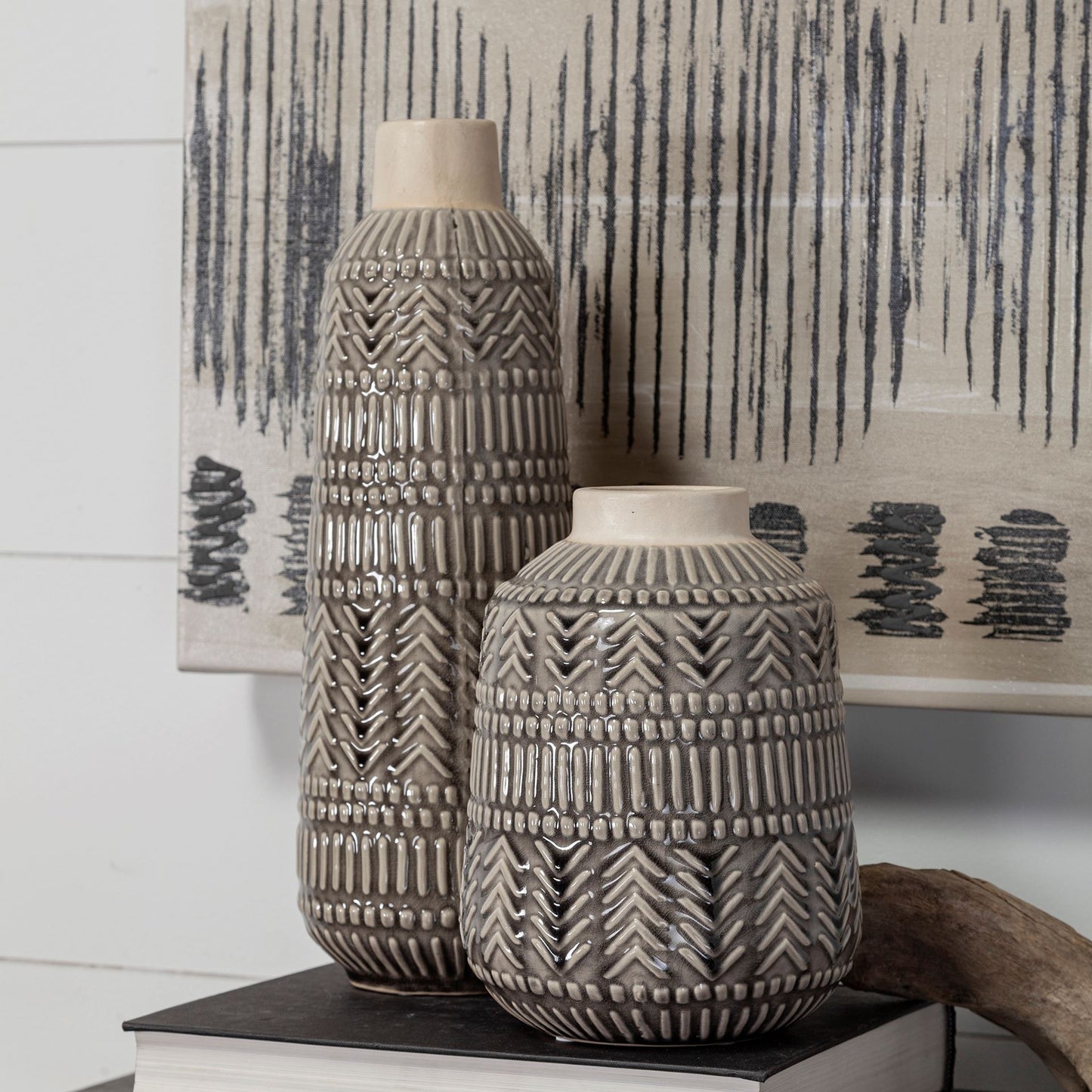 Two textured ceramic vases on a surface with a decorative wall in the background