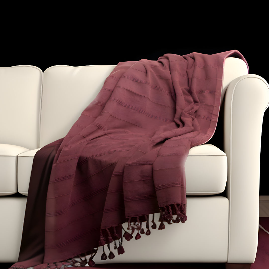 Maroon blanket with tassels draped over a white sofa against a black background