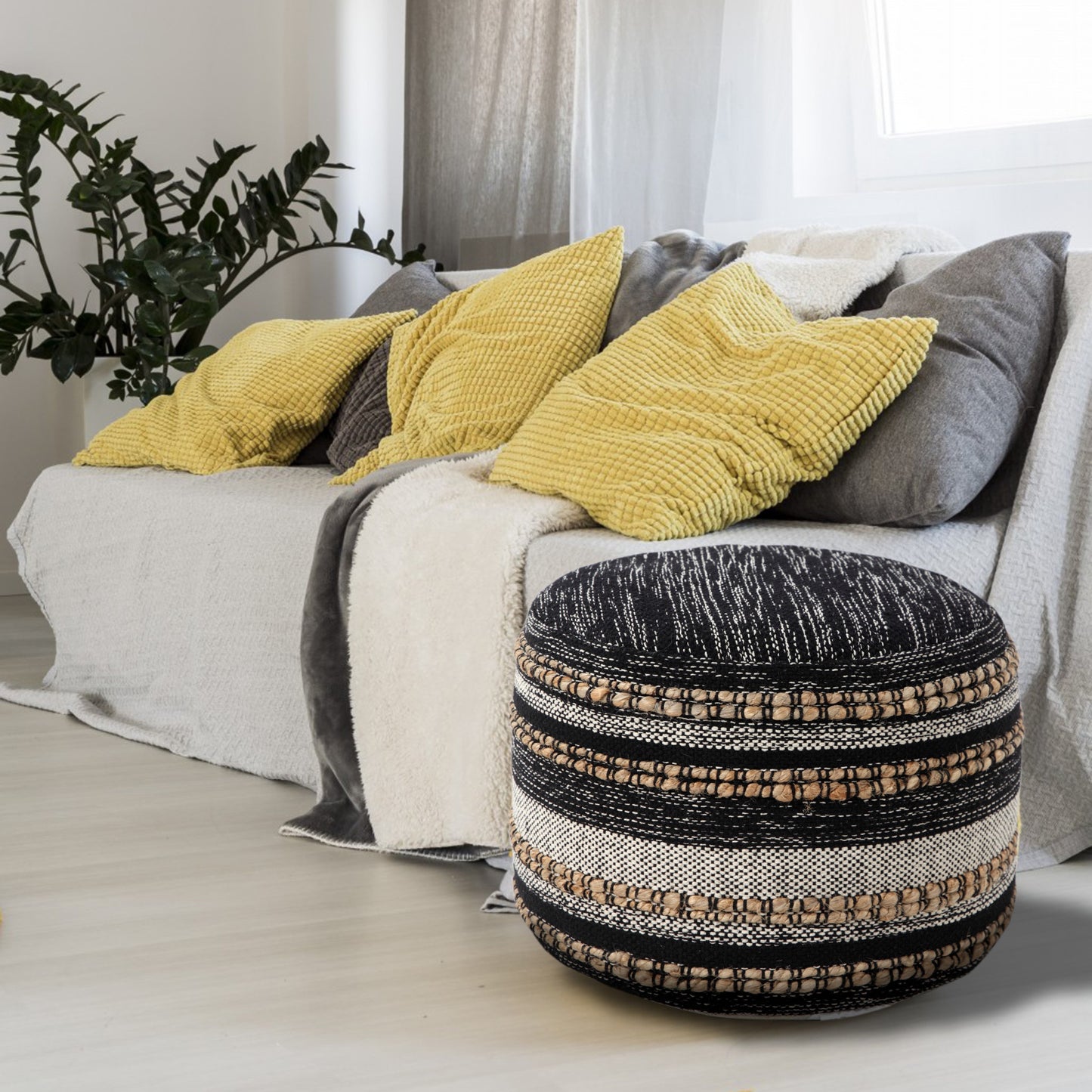 Decorative ottoman in front of a sofa with yellow and gray pillows.