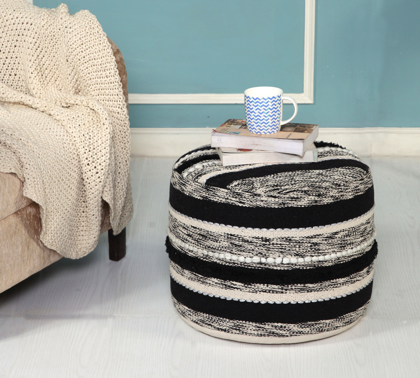 Black and white striped ottoman with a mug and books on top in a room setting.