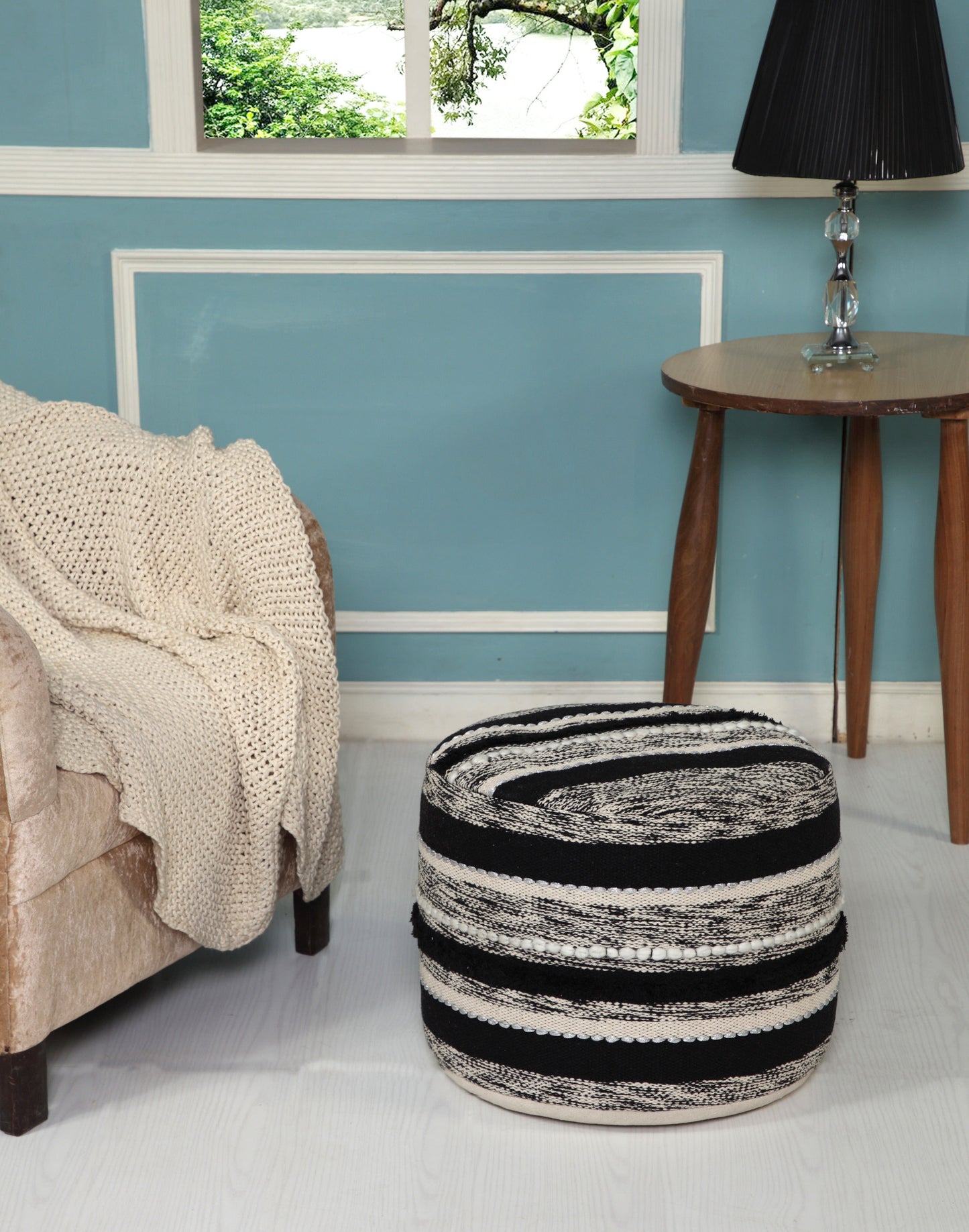 Black and white striped ottoman in a bedroom with a bed and side table.