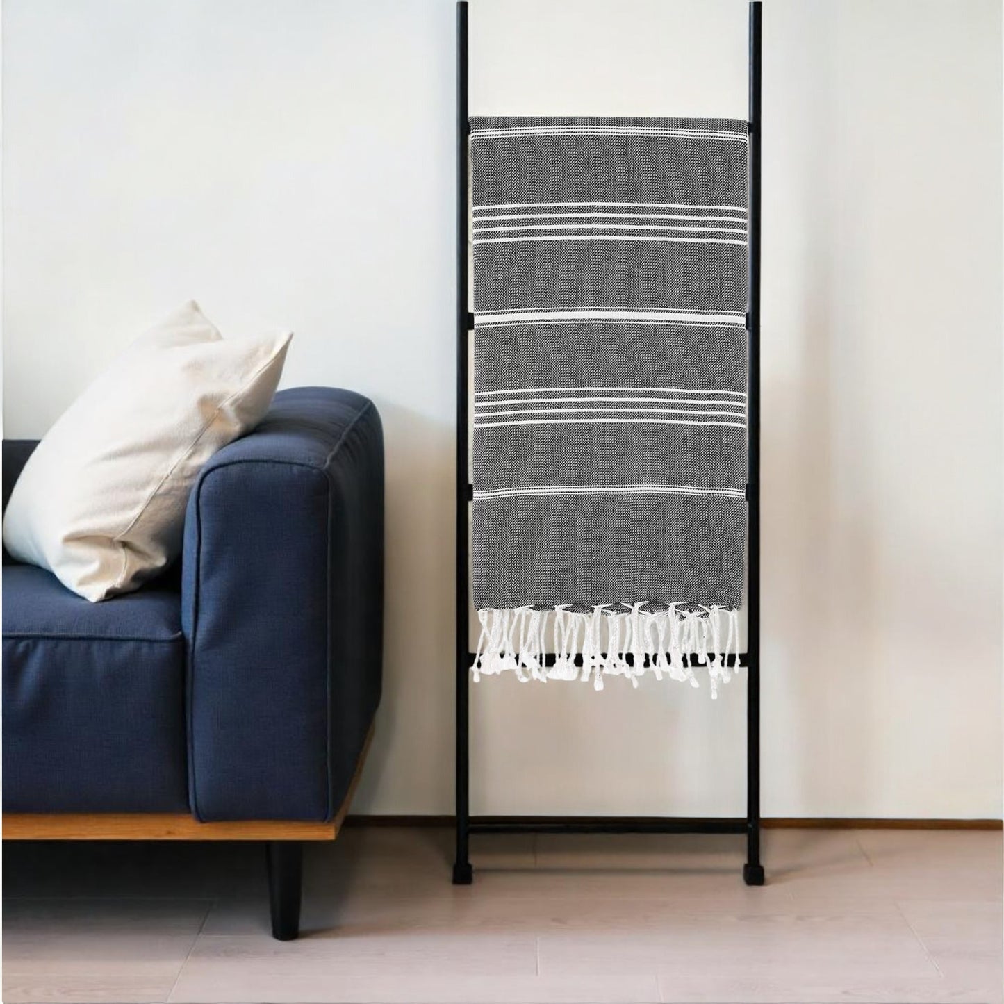 Black metal ladder with striped towel against a white wall next to a blue couch.