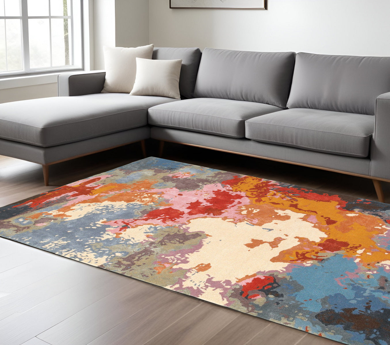 Colorful abstract rug on a wooden floor in a living room with a gray sectional sofa.