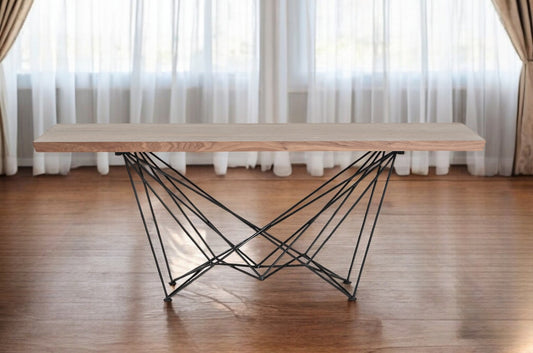 Modern coffee table with wooden top and black metal legs in a room with curtains.