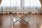 Modern coffee table with wooden top and black metal legs in a room with curtains.