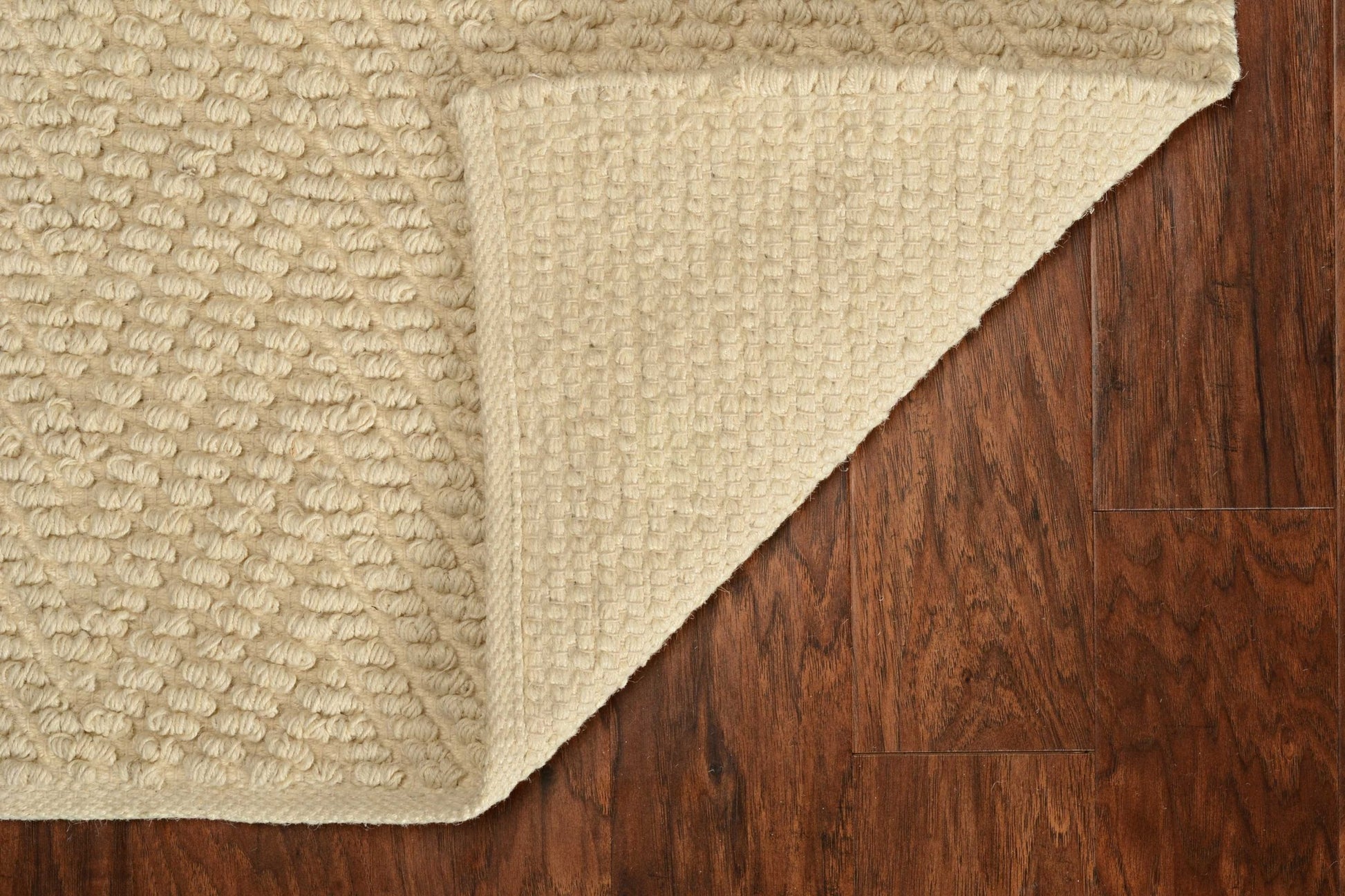 Beige textured rug corner on a wooden floor