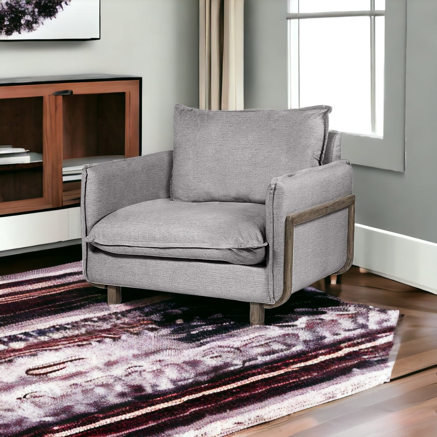 Gray armchair in a living room with a patterned rug and wooden cabinet.