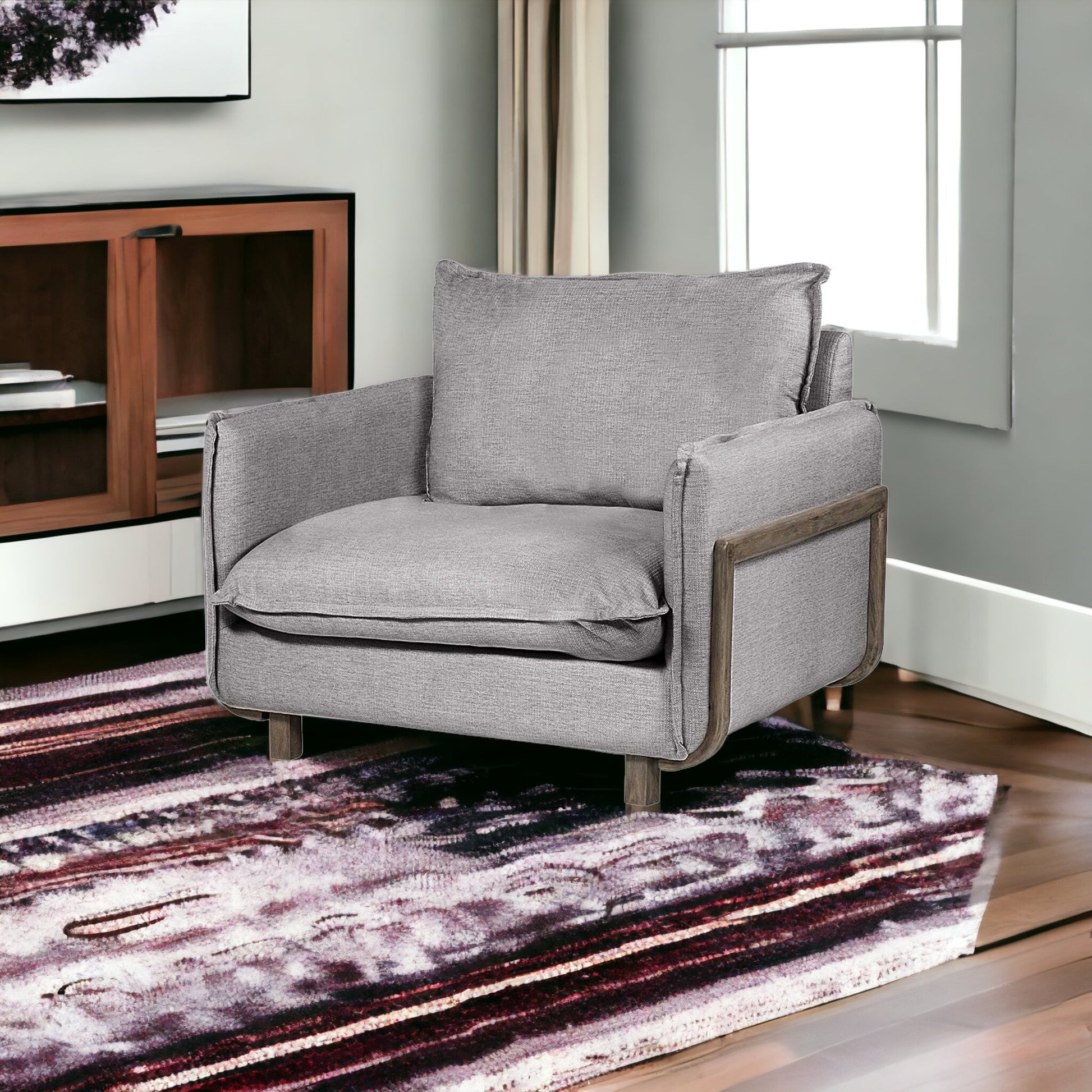 Gray armchair in a living room with a patterned rug and wooden cabinet.
