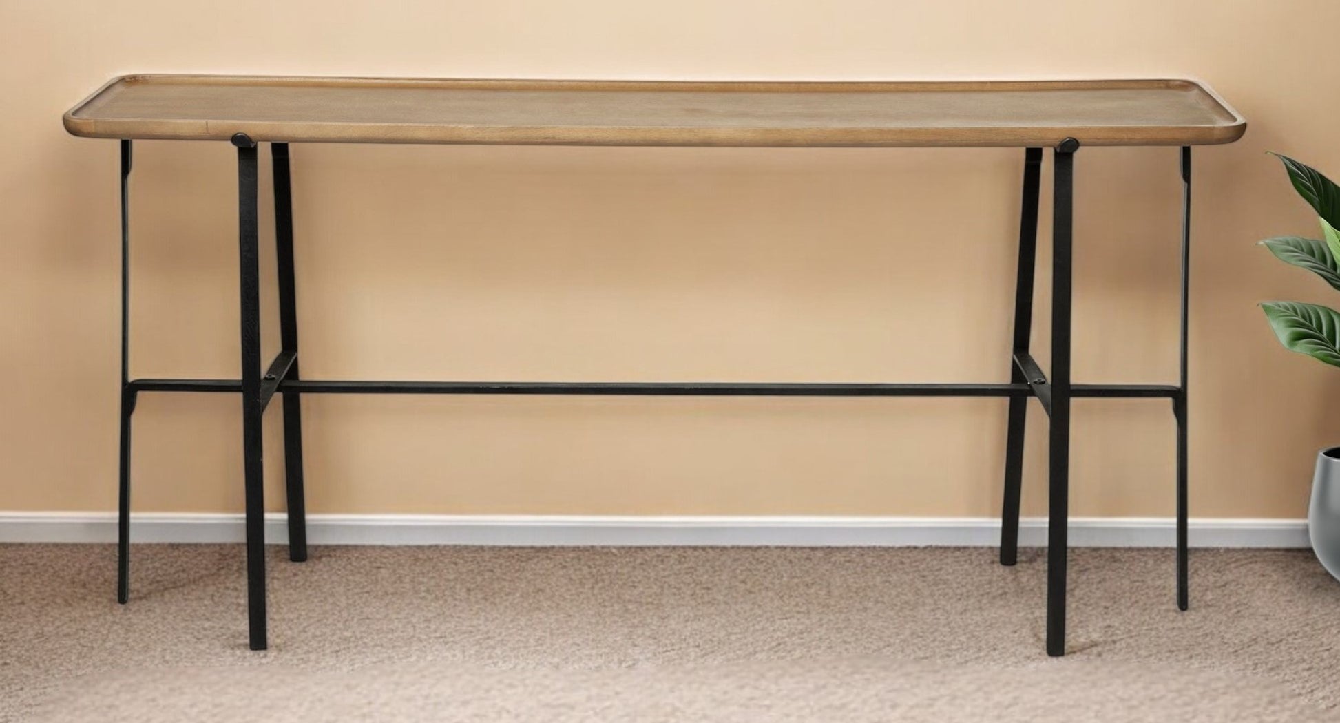 Long wooden table with black metal legs against a beige wall.