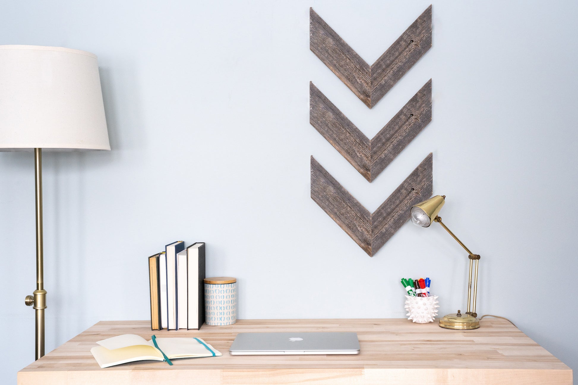 Wooden desk with decorative wall art and office supplies against a light blue wall.