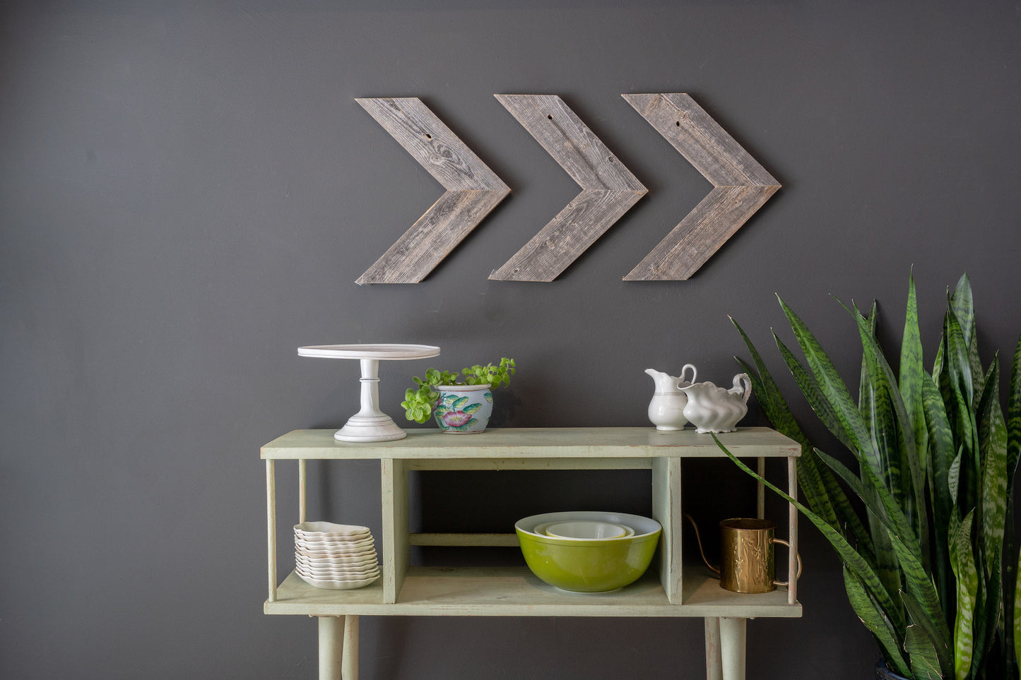 Decorative wall art with arrows above a shelf with various items against a gray wall.