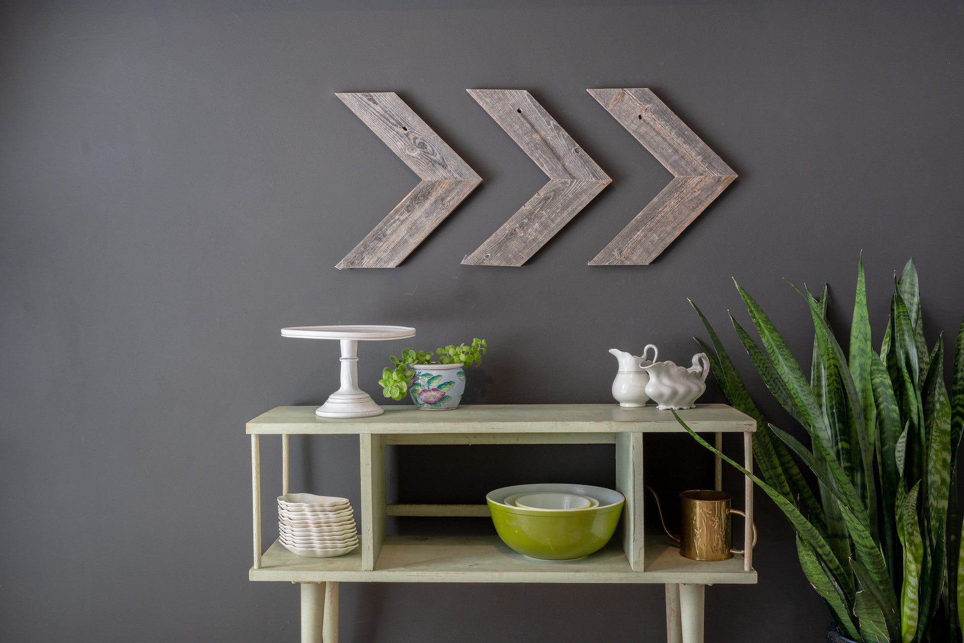 Decorative wall art with arrows above a shelf with various items against a gray wall.