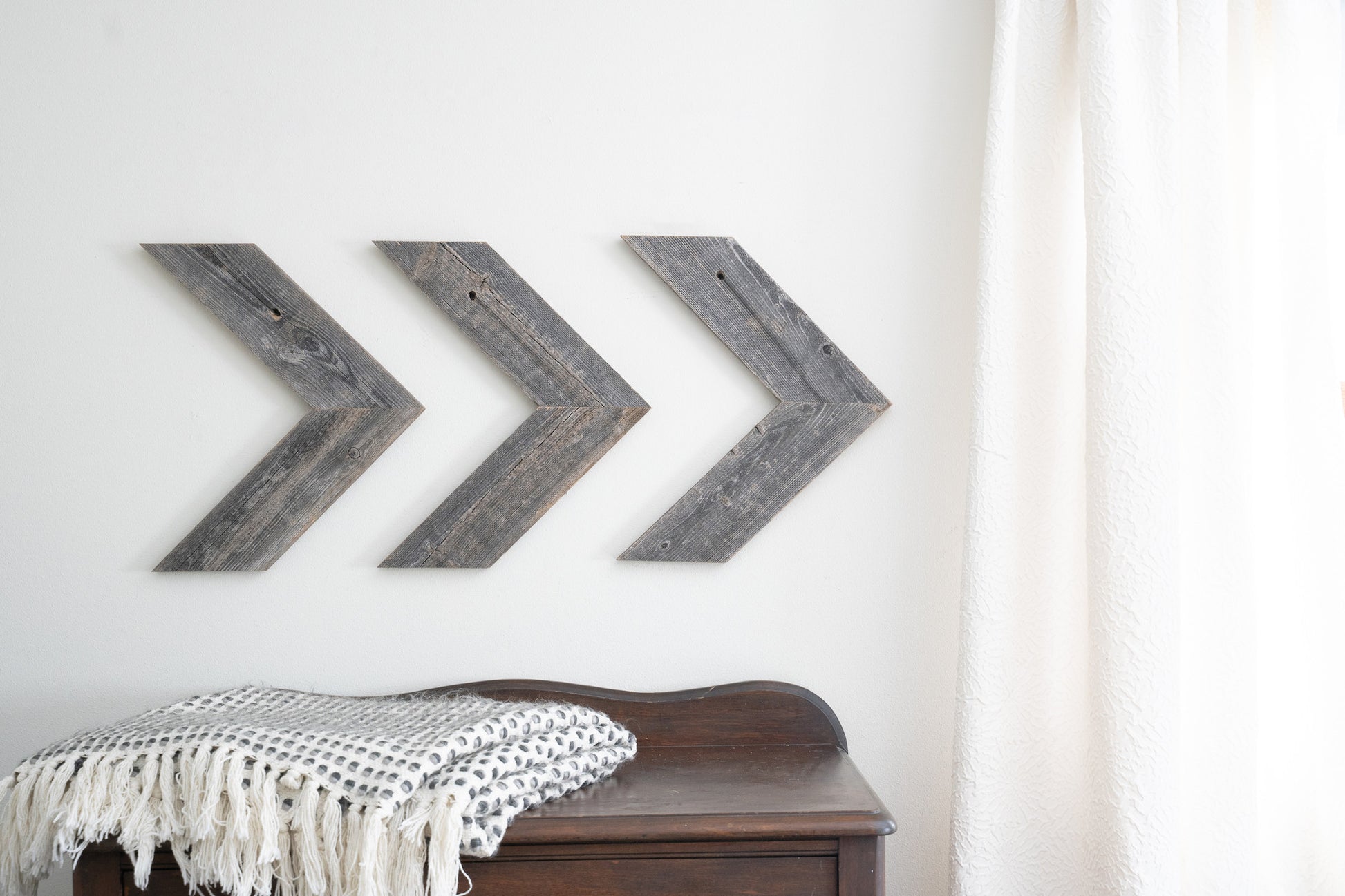 Three wooden arrow-shaped wall decorations on a white wall with a wooden bench and blanket in the foreground.