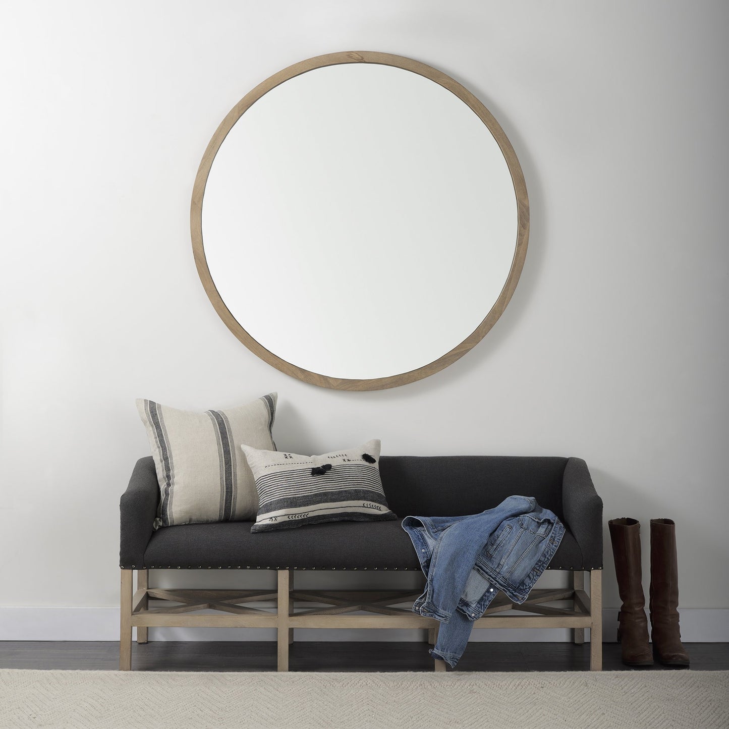 Round mirror on a white wall above a black sofa with pillows and jeans.