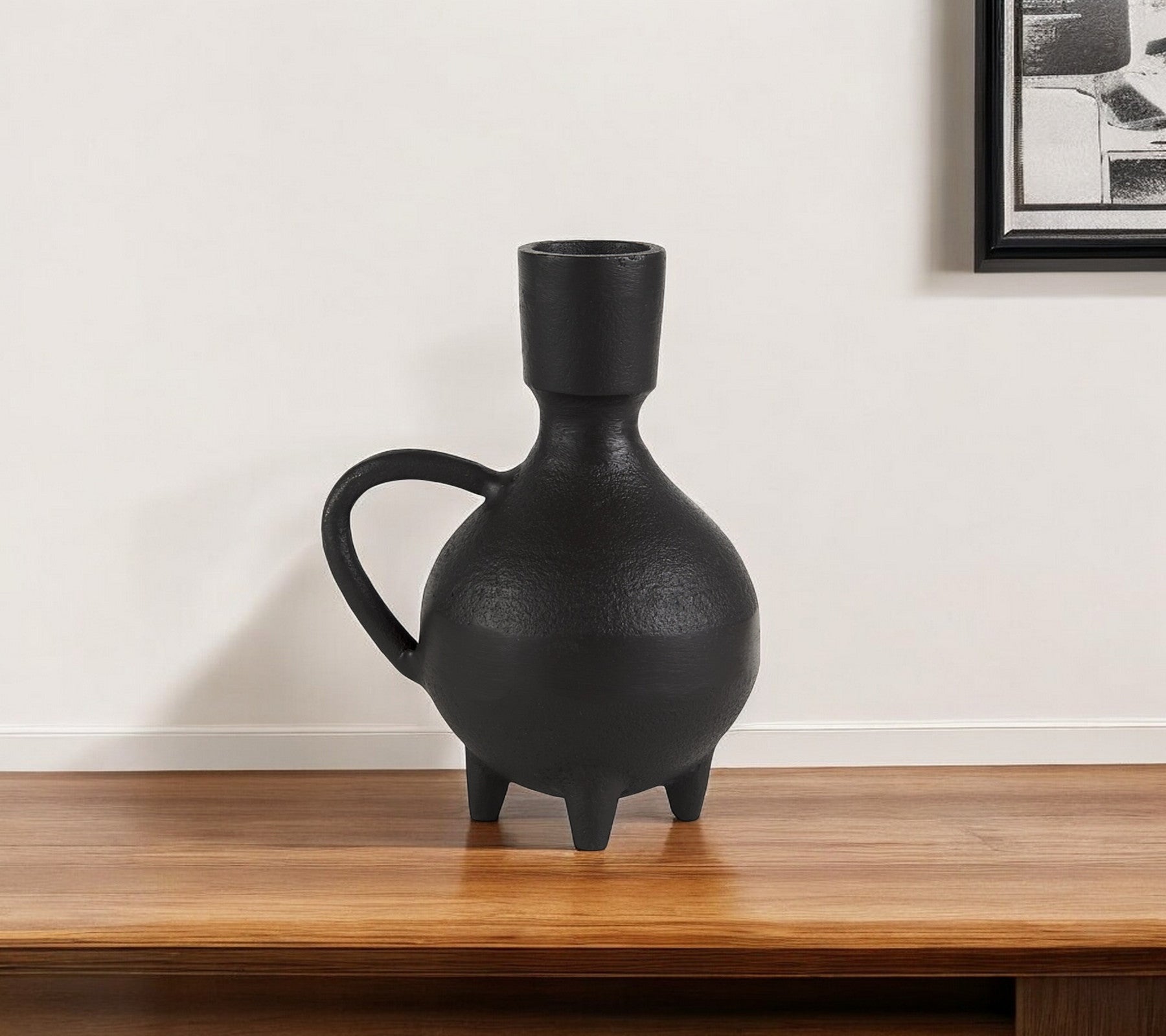 Black ceramic vase on a wooden surface with a white wall background