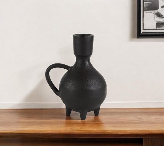Black ceramic vase on a wooden surface with a white wall background