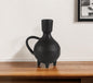 Black ceramic vase on a wooden surface with a white wall background