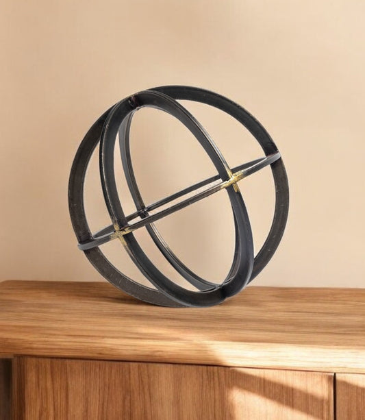 Decorative object resembling a sphere with intersecting rings on a wooden surface against a beige background