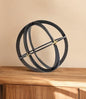 Decorative object resembling a sphere with intersecting rings on a wooden surface against a beige background