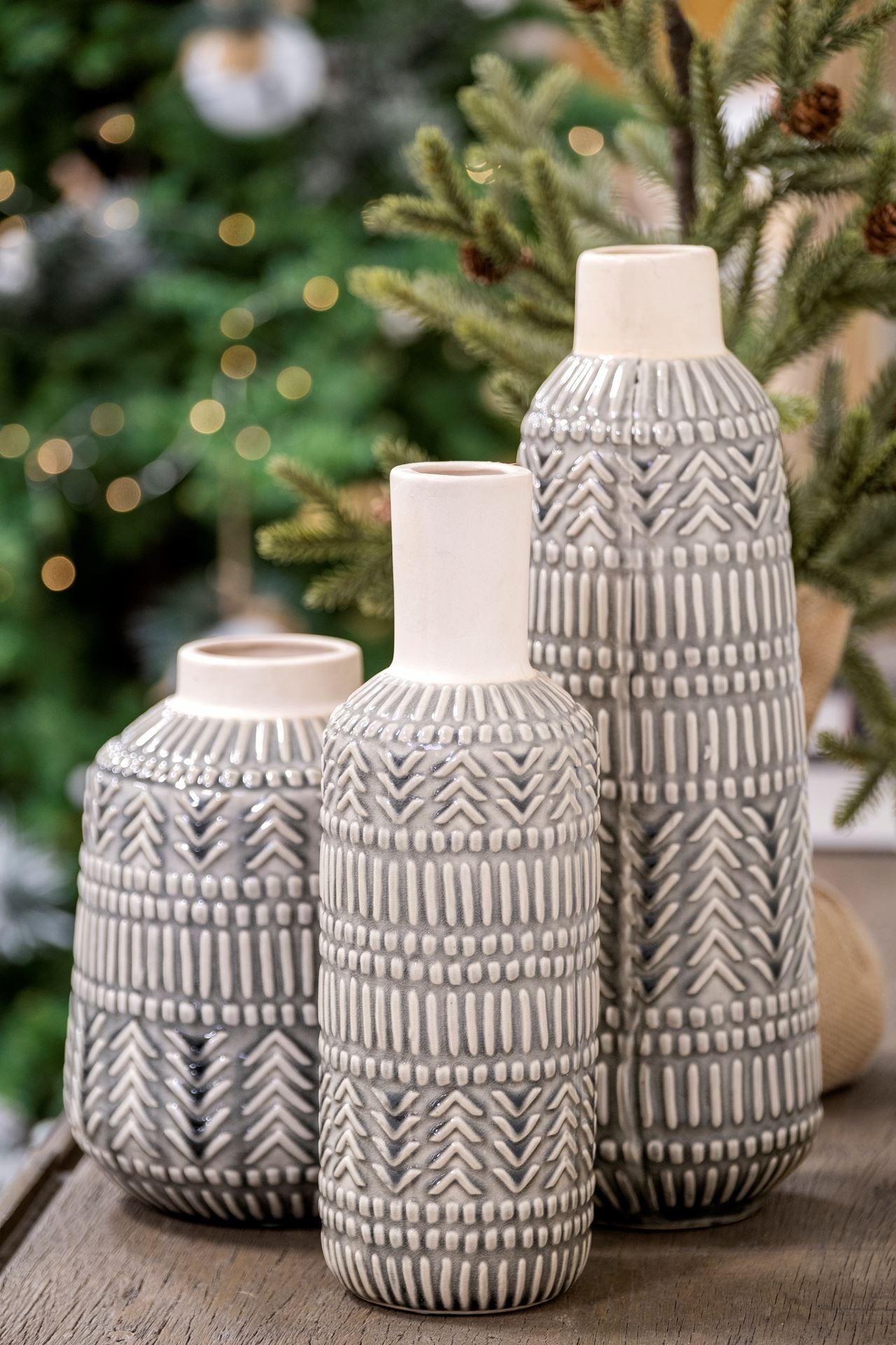 Three textured ceramic vases on a wooden surface with a blurred Christmas tree background.