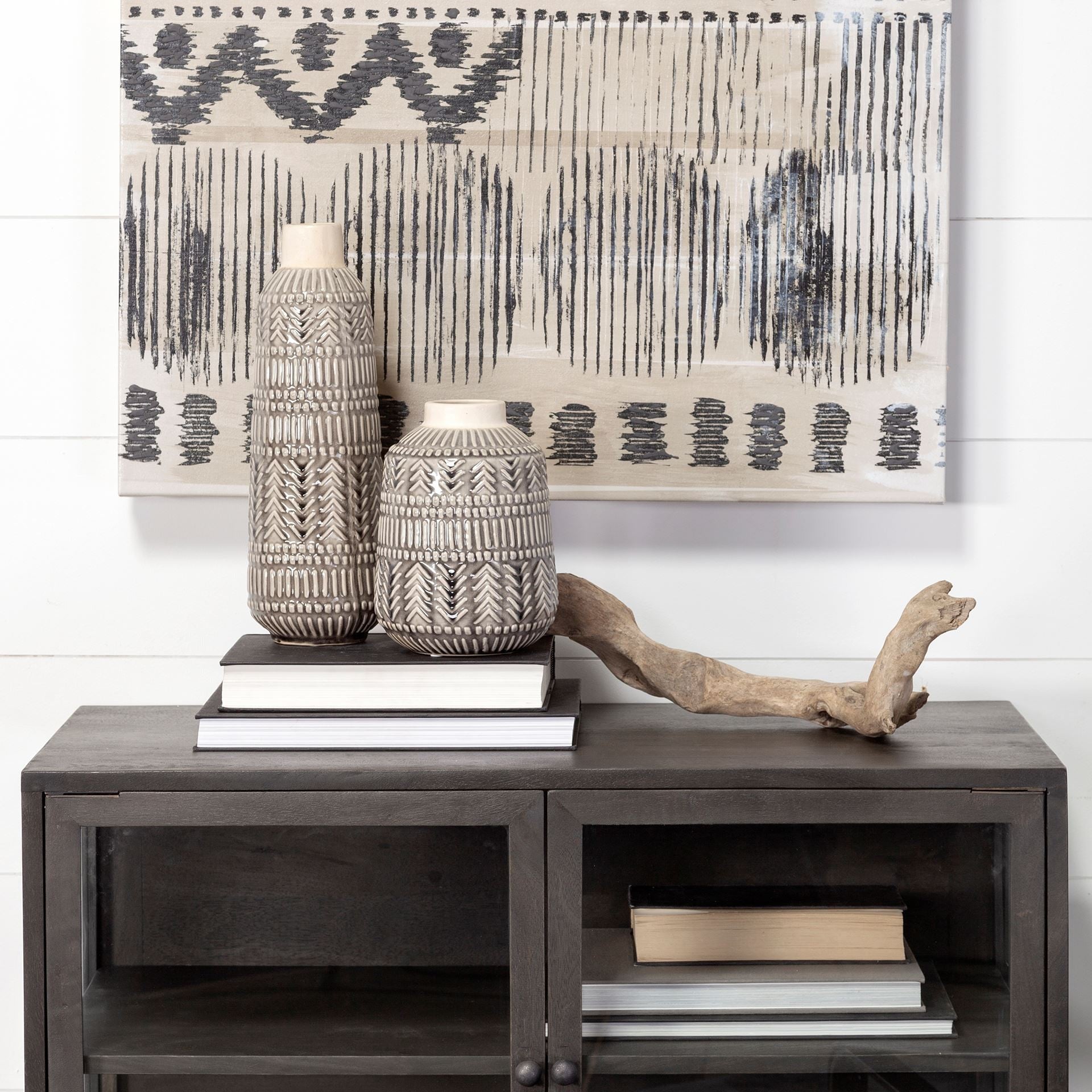 Decorative setup with vases, books, and driftwood on a wooden console table with abstract art in the background.