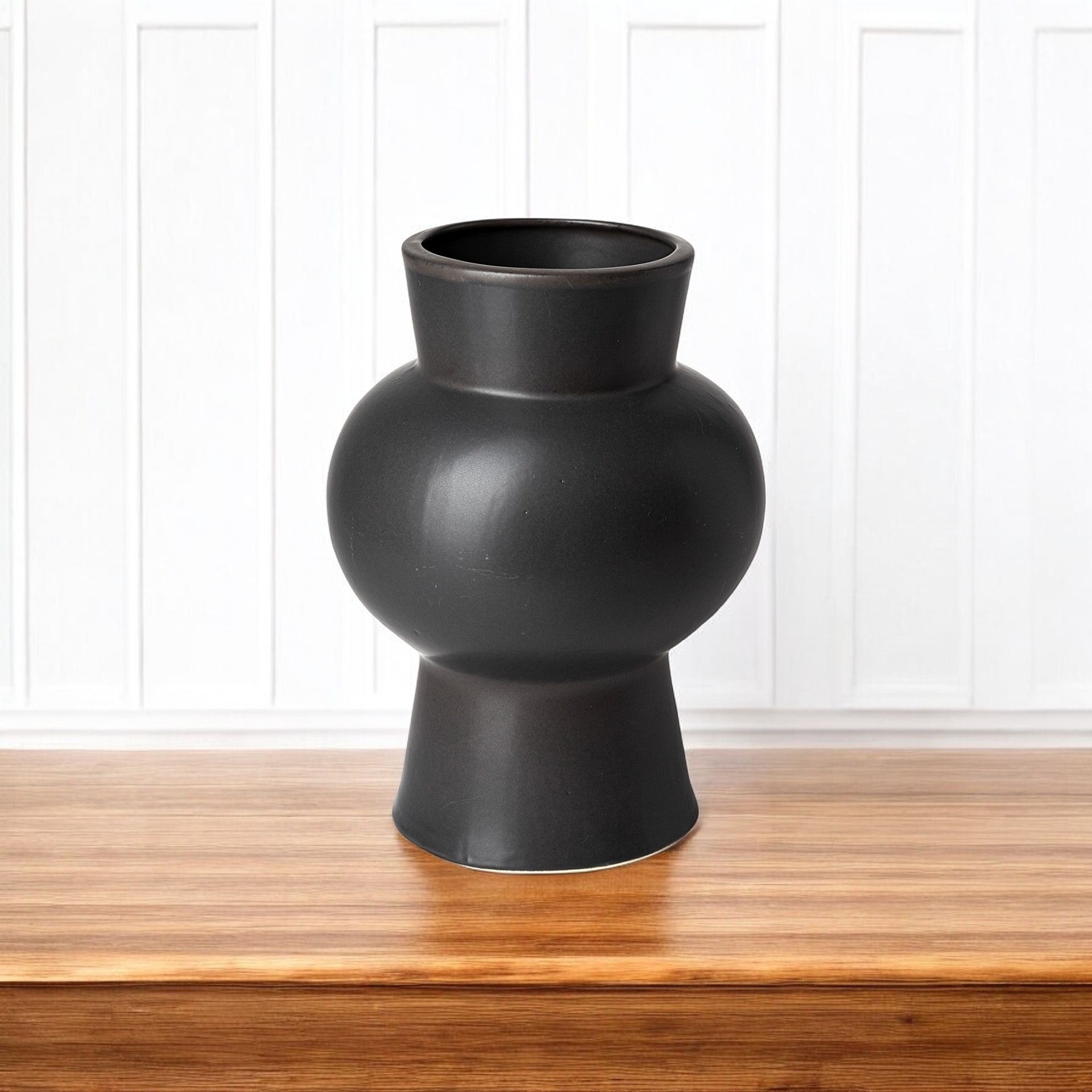 Black vase on a wooden surface with a white paneled background