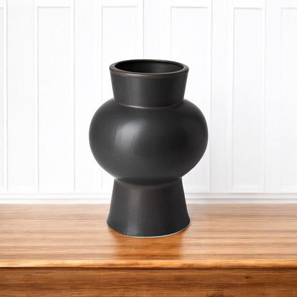 Black vase on a wooden surface with a white paneled background