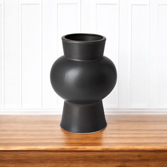 Black vase on a wooden surface with a white paneled background