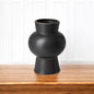 Black vase on a wooden surface with a white paneled background