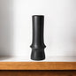 Black vase on a wooden shelf with a white background