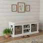 White storage bench with wicker baskets against a white wall with floral artwork.