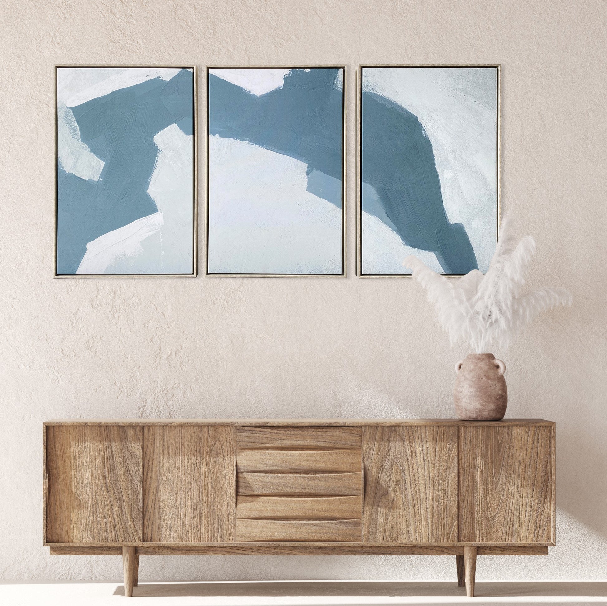 Three abstract blue artworks on a wall above a wooden sideboard.