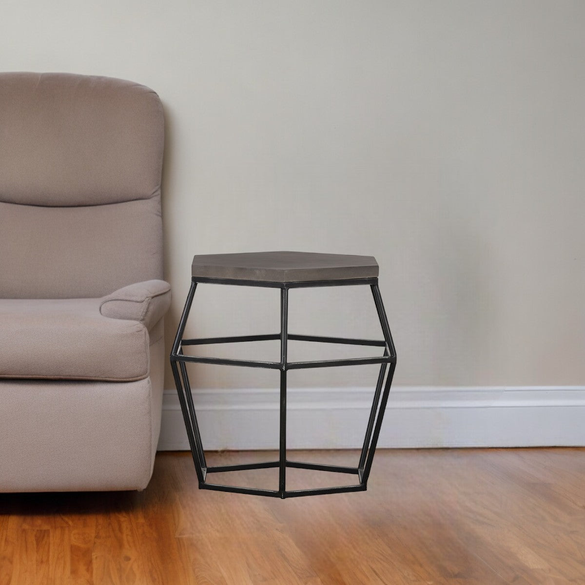 Small side table with geometric design next to a beige armchair in a room with wooden flooring and a plain wall.