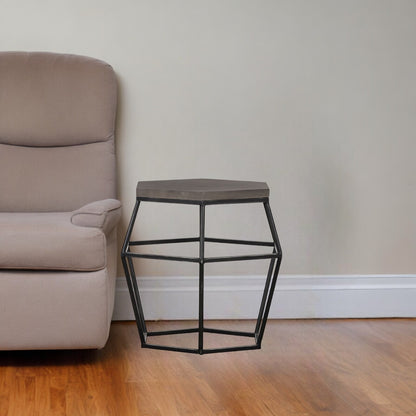 Small side table with geometric design next to a beige armchair in a room with wooden flooring and a plain wall.