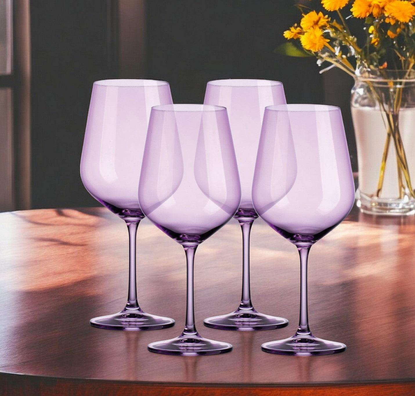 Four purple wine glasses on a wooden table with a vase of yellow flowers in the background.
