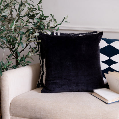 Black pillow on a beige sofa with a plant and book in the background