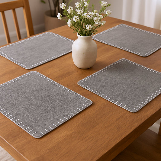 Set of gray placemats on a wooden table with a vase of flowers.