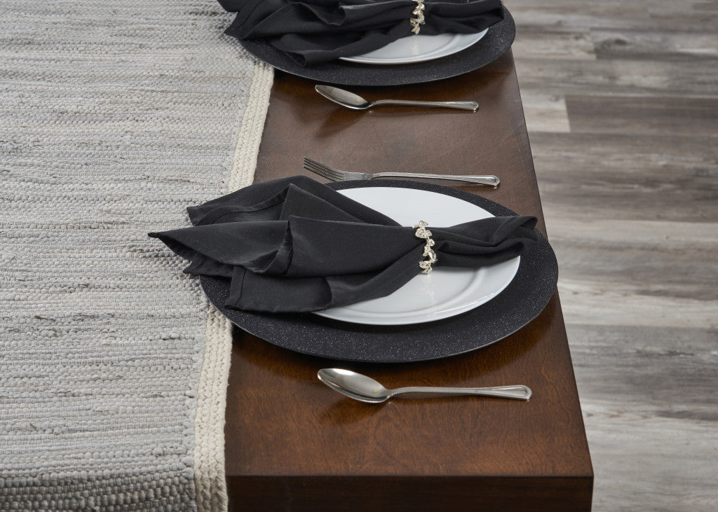 Dining table setting with black napkins, white plates, and silverware on a wooden table.