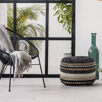 Decorative ottoman with a patterned design in a room with a chair and plants.