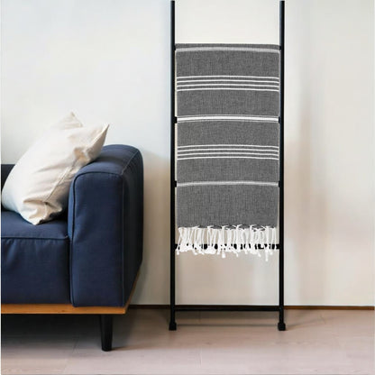 Black metal ladder with striped towel against a white wall next to a blue couch.