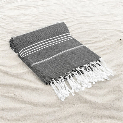 Gray towel with white stripes and fringes on a sandy surface