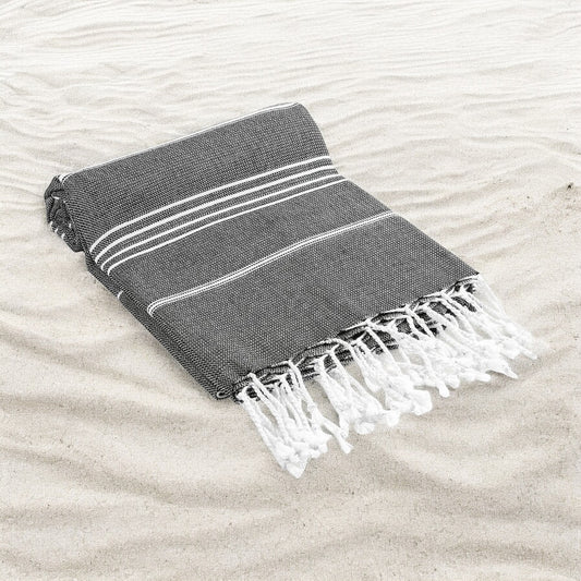 Gray towel with white stripes and fringes on a sandy surface